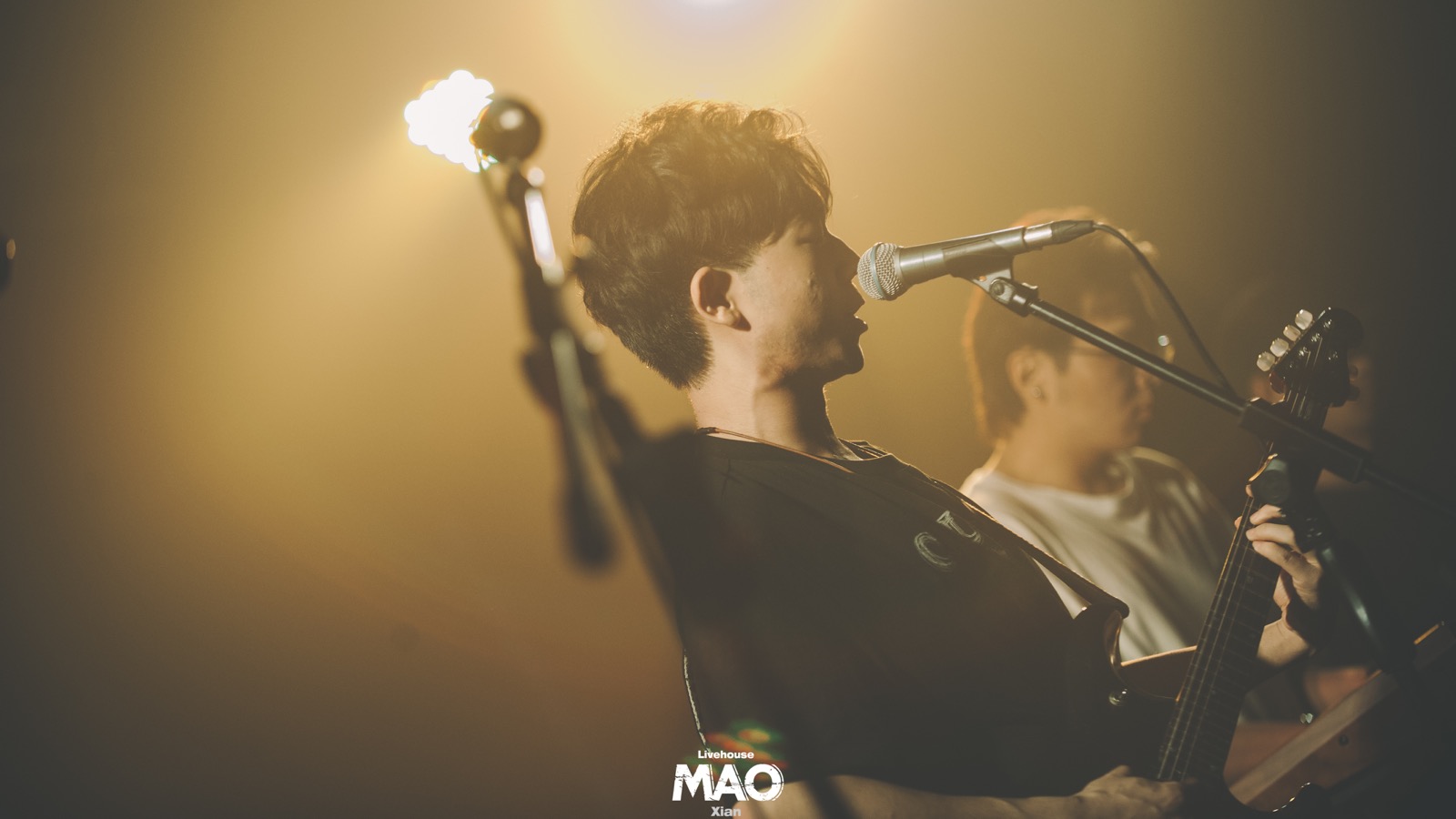 Older vocalist and guitarist under warm lights