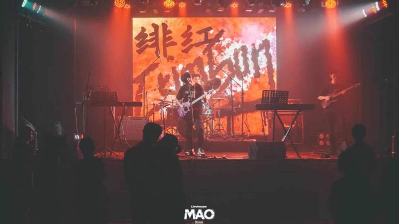 Older full-band stage performance with backdrop